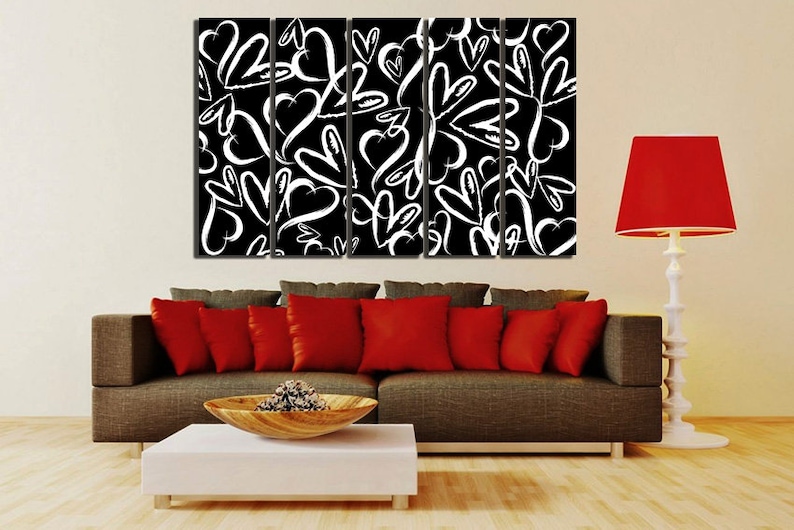 Puede incluir: Una impresi&oacute;n de arte de pared de lienzo en blanco y negro con un patr&oacute;n repetitivo de corazones blancos sobre un fondo negro. La impresi&oacute;n est&aacute; dividida en cinco paneles y se muestra sobre un sof&aacute; marr&oacute;n con almohadas rojas.
