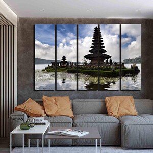 May include: A multi-panel canvas print featuring a scenic view of a traditional Balinese temple, Pura Ulun Danu Bratan, on a lake surrounded by lush greenery. The temple is a striking silhouette against a cloudy sky, reflected in the water.