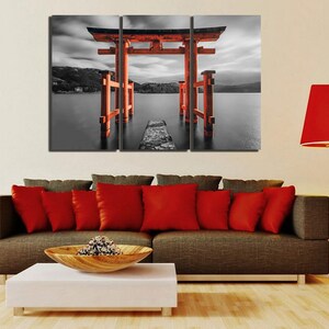May include: A three-panel canvas print featuring a red Japanese torii gate, a traditional gateway to Shinto shrines, standing in a body of water. The gate is surrounded by a black and white landscape, creating a striking contrast.