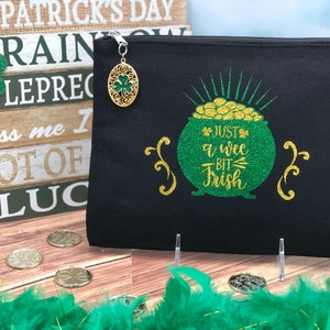 May include: Black canvas zippered pouch with a gold pot of gold design and the text "Just a wee bit Irish". The pouch has a gold charm with a shamrock design.