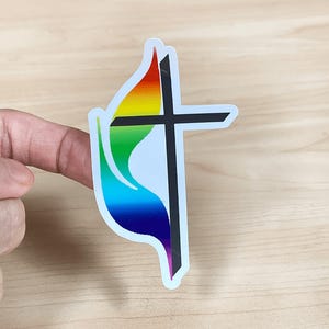 May include: A sticker featuring a black cross and a flame design with rainbow colors. The flame transitions from red to purple, with green and yellow in between. The sticker has a white border.