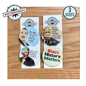 May include: Four circular pin-back buttons featuring historical figures and text. One shows Martin Luther King Jr. with the text 'The time is always right to do what is right'. Another shows John Lewis with 'Get in trouble good trouble necessary trouble'. A third shows Frederick Douglass with 'There is no progress without struggle'. The fourth button reads 'Black History Matters' in red and green text.