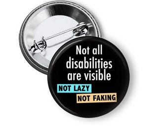 May include: A black button pin with the text "Not all disabilities are visible." The pin also includes the phrases "NOT LAZY" in a blue box and "NOT FAKING" in a tan box. The pin has a silver metal backing.