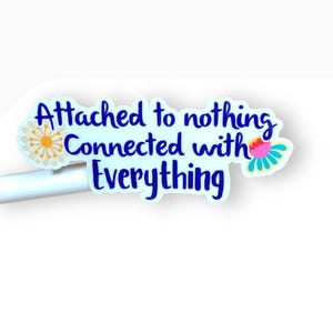 May include: White sticker with blue text that reads "Attached to nothing Connected with Everything". The sticker has two colorful flower illustrations on either side of the text.