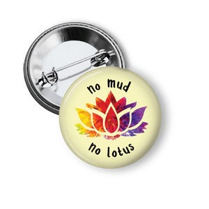 May include: A round button with a pin back. The button has a light yellow background with a colorful lotus flower design in shades of red, orange, yellow, and purple. The text "no mud no lotus" is printed in black.