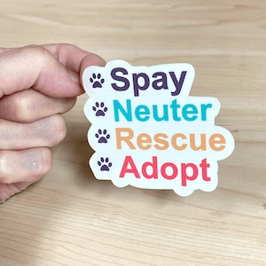 May include: A white sticker with the words "Spay, Neuter, Rescue, Adopt" in purple, teal, orange, and red, with paw prints. The sticker is held by a hand.