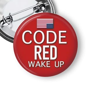 May include: A red button with the text "CODE RED WAKE UP" in white. The button features a small American flag graphic at the top. The pin has a silver metal backing.