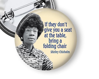 May include: A round button pin featuring a black and white portrait of Shirley Chisholm, with the quote "If they don't give you a seat at the table, bring a folding chair." The pin has a silver metal backing.