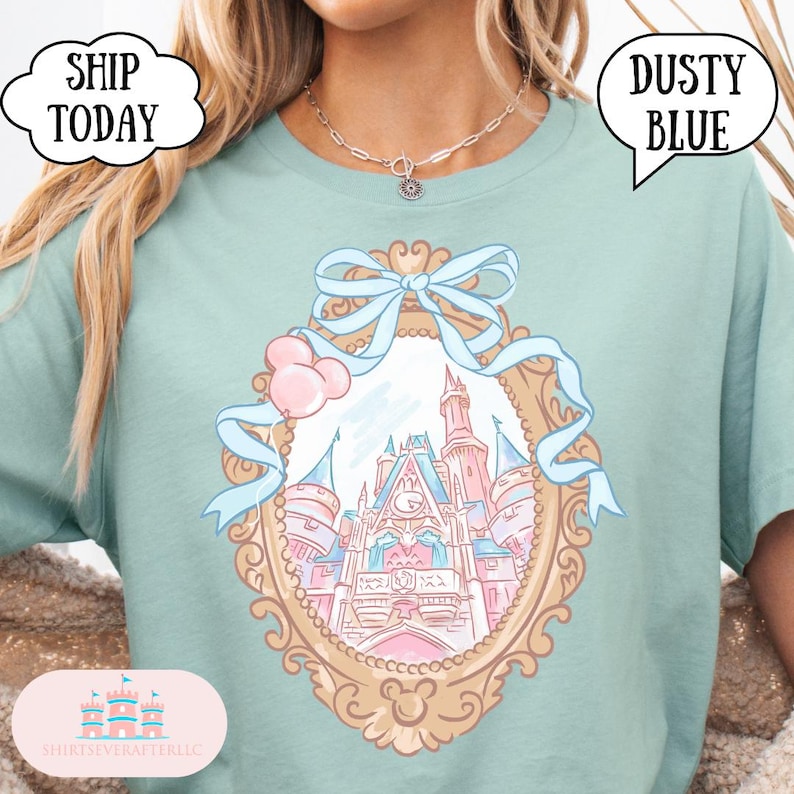 Puede incluir: Camiseta azul polvoriento con un dise&ntilde;o de castillo de cuento de hadas dentro de un marco dorado adornado, adornado con un lazo azul claro y globos rosas. La camiseta tiene el texto "Dusty Blue" y "Ship Today".