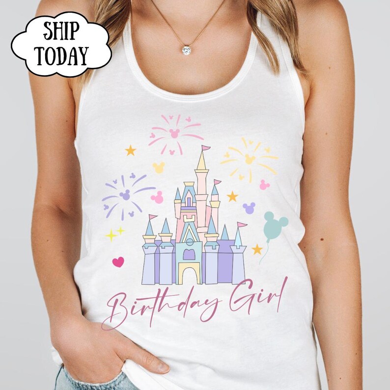 May include: White vest top with a colourful castle graphic, fireworks, stars, and Mickey Mouse silhouettes. The text "Birthday Girl" is written in a cursive font. The top is sleeveless.