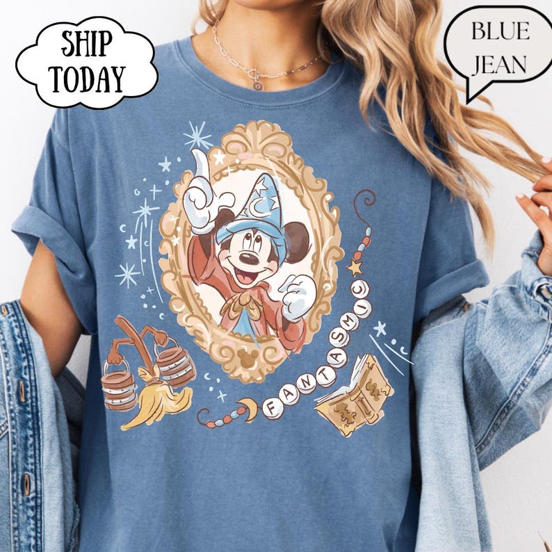 K&ouml;nnte beinhalten: Blaues T-Shirt mit einem gerahmten Bild von Mickey Mouse in einem Zauberer-Outfit. Das Design enth&auml;lt das Wort "FANTASMIC" und andere magische Elemente. Das T-Shirt hat hochgekrempelte &Auml;rmel und den Text "BLUE JEAN".