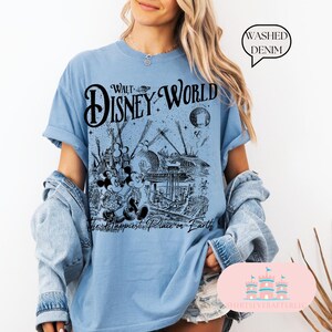 May include: Light blue t-shirt with a black and white graphic of Walt Disney World, featuring Mickey and Minnie Mouse, a castle, and other park attractions. Text on the shirt reads "Walt Disney World" and "The Happiest Place on Earth."