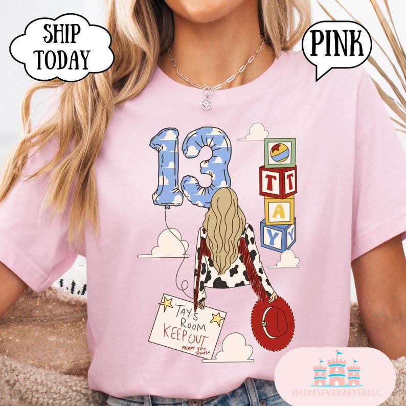 May include: A light pink t-shirt featuring a graphic of a person with long blonde hair wearing a cow-print jacket with red fringe. The design includes a blue cloud-patterned balloon shaped like the number 13, alphabet blocks, and a sign reading TAY'S ROOM KEEP OUT.