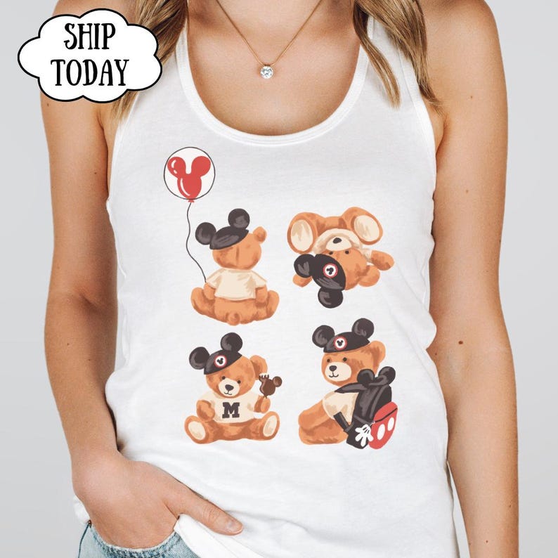 May include: A white tank top featuring a graphic print of four brown teddy bears wearing black mouse ear hats. One bear holds a red balloon, another wears a shirt with the letter M, and one carries a black backpack with red accents. The text SHIP TODAY is visible.