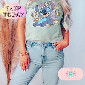May include: A light green t-shirt with a blue cartoon character surrounded by flowers and hearts. The character is smiling and has a peace sign on its head. The text "SHIP TODAY" is in a white cloud in the top left corner of the image.