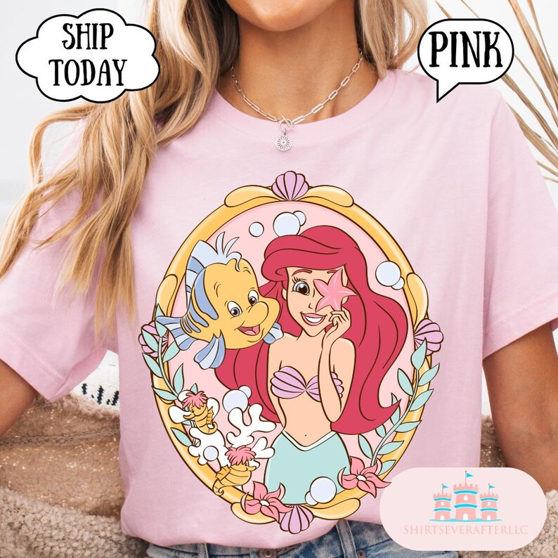 May include: Pink t-shirt featuring a cartoon illustration of Ariel from The Little Mermaid, holding a starfish with Flounder. The design is framed in a gold oval with seashells and flowers. The text "SHIP TODAY" and "PINK" are in speech bubbles.