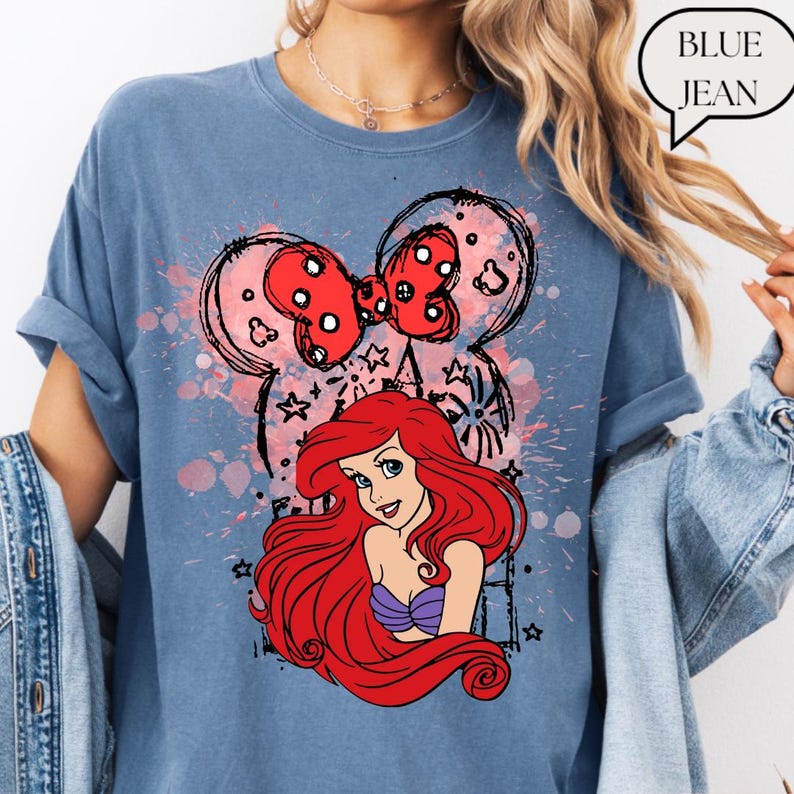 May include: Blue jean colored t-shirt featuring a graphic of Ariel from The Little Mermaid with a red bow and Mickey Mouse ears. The text "BLUE JEAN" is in a speech bubble.