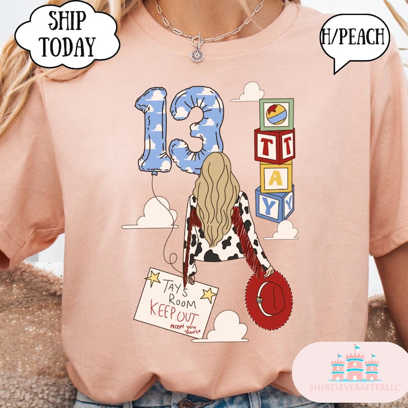 May include: A peach-colored t-shirt featuring a graphic of a person with long blonde hair, a cow-print jacket with red fringe, and a red hat. The design includes a blue cloud-patterned number 13 balloon, alphabet blocks, and a sign reading TAY'S ROOM KEEP OUT except you travis.