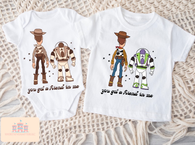 May include: Two white t-shirts featuring a cartoon image of Woody and Buzz Lightyear from Toy Story. The shirts have the text "you got a friend in me" printed on them.