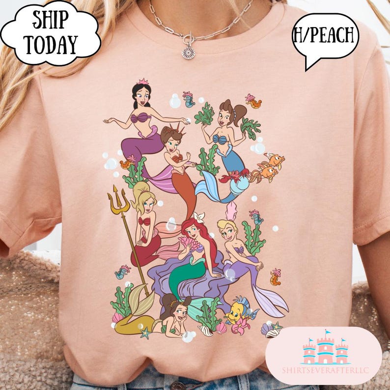 Op de afbeelding: Perzikkleurig T-shirt met een kleurrijke illustratie van verschillende zeemeerminnen met verschillende haarkleuren en outfits. Het ontwerp bevat een drietand, vissen en zeewier. Tekst op het shirt zegt "SHIP TODAY" en "H/PEACH".
