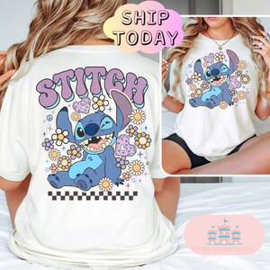 May include: White t-shirt with a blue Stitch character from Lilo & Stitch surrounded by flowers and the word "STITCH" in purple letters. The shirt has a checkered pattern at the bottom.