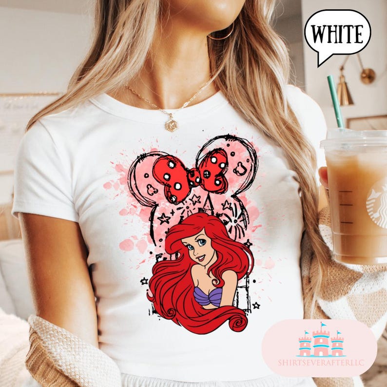 May include: White t-shirt featuring a graphic of Ariel from The Little Mermaid, with a Minnie Mouse-inspired bow and ears design. The design includes pink watercolor splashes and star accents. The word "WHITE" is in a speech bubble.