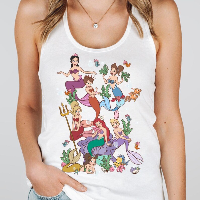 Op de afbeelding: Witte tanktop met een kleurrijke illustratie van verschillende zeemeerminnen met verschillende haarkleuren en zeemeerminstaarten. De zeemeerminnen zijn omringd door zeegroenten, vissen en bellen. Het ontwerp is in cartoonstijl.