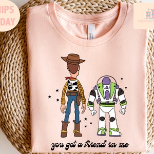 May include: Pink t-shirt featuring a cartoon image of Woody and Buzz Lightyear from Toy Story. The text "you got a friend in me" is printed below the characters.