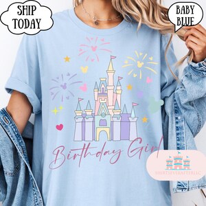 May include: Pale blue t-shirt with a castle graphic, fireworks, hearts, and stars. The words "Birthday Girl" are in a script font. The shirt also has the text "Ship Today" in a cloud-shaped bubble.