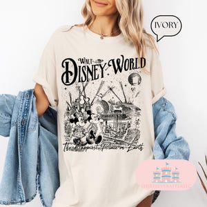 May include: Ivory-colored t-shirt featuring a black and white graphic of Walt Disney World. The design includes Mickey and Minnie Mouse, iconic park structures, and the text "Walt Disney World" and "The Happiest Place on Earth."