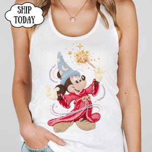 May include: White vest top with a graphic of Mickey Mouse as a sorcerer, holding a magic wand. Mickey is wearing a blue hat and a red robe. The text "SHIP TODAY" is in a cloud-shaped bubble.