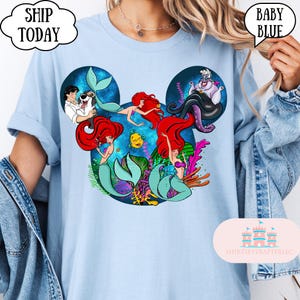 Puede incluir: Camiseta de manga larga azul beb&eacute; con un gr&aacute;fico de Ariel y otros personajes de La Sirenita, dispuestos en una silueta de Mickey Mouse. La camiseta tiene las palabras "Ship Today" y "Baby Blue" impresas.