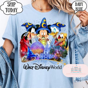 May include: Baby blue t-shirt featuring a colorful graphic of Mickey Mouse, Goofy, Donald Duck, and Pluto wearing wizard hats. The graphic includes the text "Walt Disney World" and a castle. The shirt has the text "Ship Today" in a cloud.
