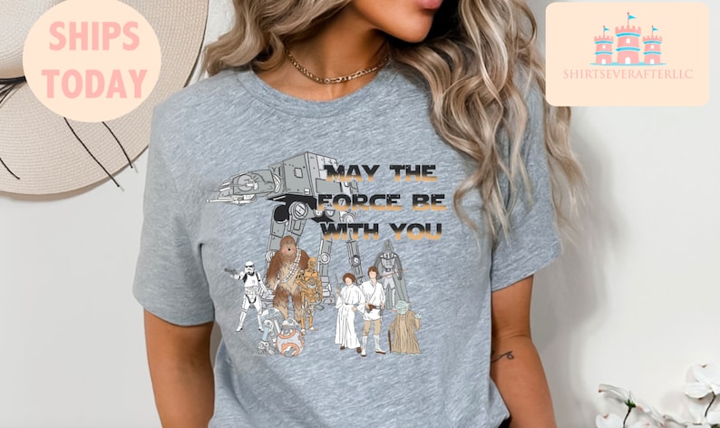 Puede incluir: Camiseta gris con un gr&aacute;fico de personajes de Star Wars, incluyendo Chewbacca, Darth Vader, Yoda y R2-D2. El texto "Que la fuerza te acompa&ntilde;e" est&aacute; impreso en la camiseta.