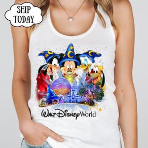 May include: White tank top featuring a colorful graphic of Mickey Mouse, Donald Duck, Goofy, and Pluto wearing wizard hats. The graphic includes the text "Walt Disney World" and a castle illustration.