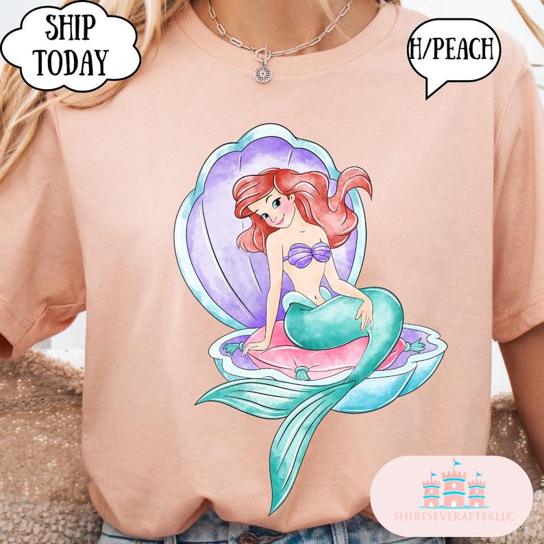 May include: Peach-coloured t-shirt with a colourful illustration of a mermaid in an open seashell. The mermaid has red hair, a purple seashell bra, and a teal tail. The text "SHIP TODAY" is in a speech bubble.