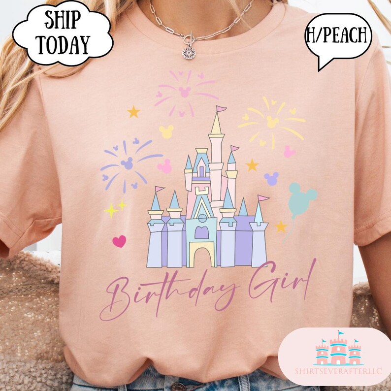 May include: Peach-coloured t-shirt with a castle graphic, fireworks, and Mickey Mouse silhouettes. The text "Birthday Girl" is in script. The shirt has a round neckline. The colour is described as (H/Peach).
