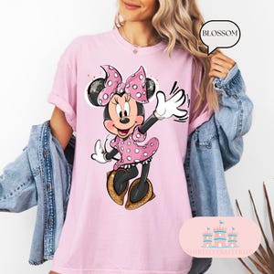 Puede incluir: Camiseta rosa con un gr&aacute;fico de Minnie Mouse con un vestido de lunares rosa y blanco y un lazo rojo. El texto "BLOSSOM" est&aacute; en un bocadillo de di&aacute;logo blanco.