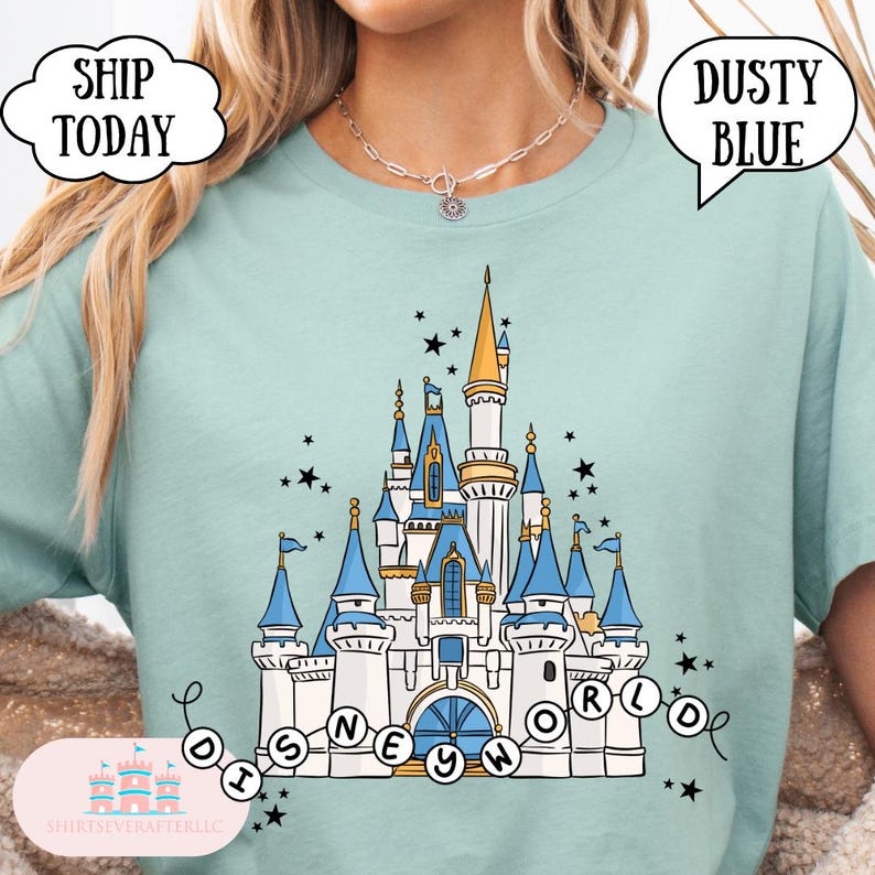 May include: Dusty blue t-shirt featuring a detailed illustration of a castle with blue and gold accents, surrounded by stars. The text "DISNEYWORLD" is displayed below the castle. The shirt also has the text "SHIP TODAY" and "DUSTY BLUE".