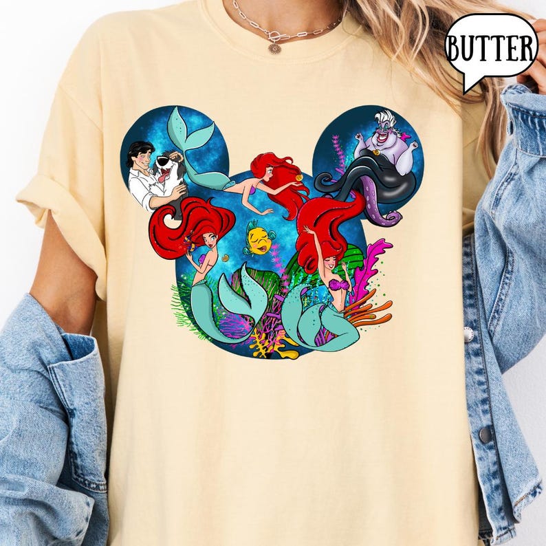 Puede incluir: Camiseta amarillo claro con un dise&ntilde;o de los personajes de La Sirenita de Disney dispuestos en forma de cabeza de Mickey Mouse. El dise&ntilde;o incluye a Ariel, el Pr&iacute;ncipe Eric, &Uacute;rsula y Flounder.