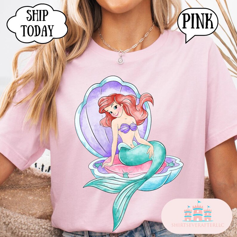May include: Pale pink t-shirt with a mermaid illustration in a seashell. The mermaid has red hair and a teal tail. The shirt has the text "PINK" and "SHIP TODAY".