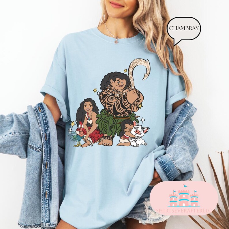 May include: Light blue t-shirt with a graphic print of Maui, Moana, and Pua from the Disney movie Moana. The text "CHAMBRAY" is in a speech bubble above the graphic.