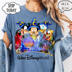 May include: Blue t-shirt featuring Mickey Mouse, Goofy, Donald Duck, and Pluto with a castle and the text "Walt Disney World." The characters wear wizard hats. The shirt has rolled-up sleeves.