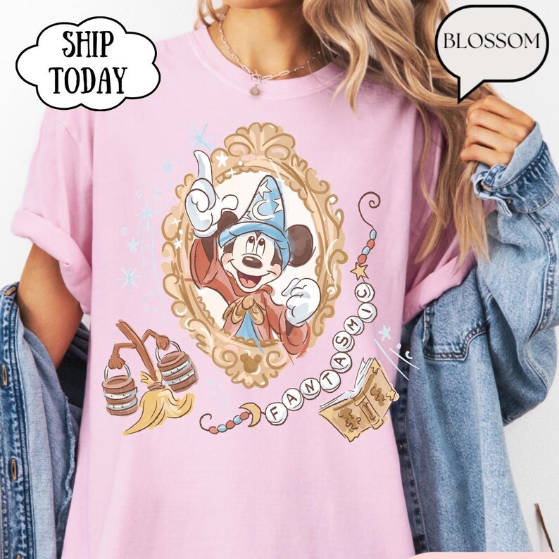 K&ouml;nnte beinhalten: Hellrosa T-Shirt mit Mickey Mouse als Zauberer in einem goldenen Rahmen. Das Design enth&auml;lt das Wort "FANTASMIC" und andere magische Elemente. Das Shirt hat den Text "BLOSSOM" in einer Sprechblase.
