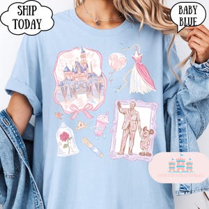 Op de afbeelding: Babyblauw T-shirt met roze en paarse illustraties, waaronder een kasteel, jurk en personages. Het shirt heeft de tekst "SHIP TODAY" en "BABY BLUE" in tekstballonnen. Het shirt heeft ook de tekst "SHIRTSEVERAFTER, LLC".