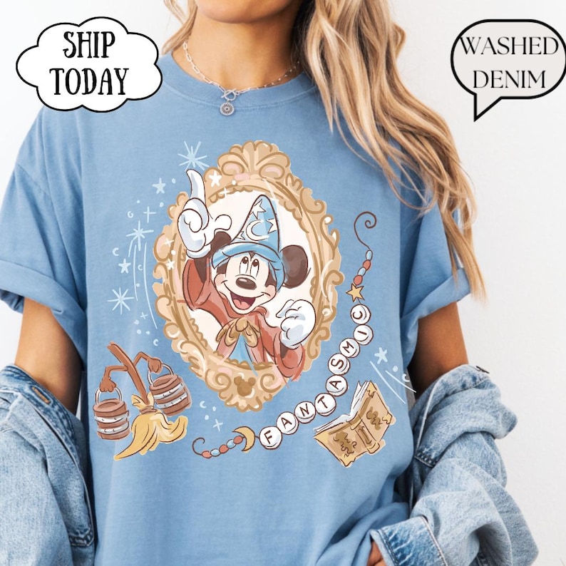 K&ouml;nnte beinhalten: Hellblaues T-Shirt mit einem Cartoon-Bild von Mickey Mouse als Zauberer in einem goldenen Rahmen. Das Shirt hat das Wort "FANTASTIC" in einem geschwungenen Design. Der Text "Washed Denim" befindet sich in einer Sprechblase. Der Text "Ship Today" befindet sich in einer Wolke.