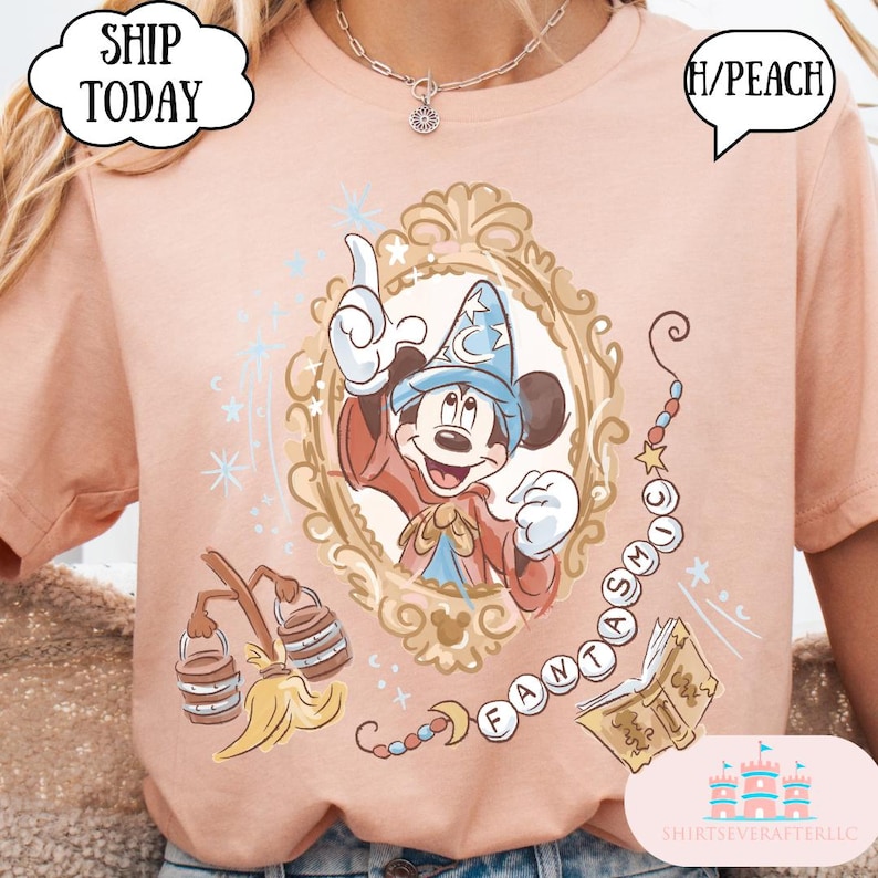 K&ouml;nnte beinhalten: Pfirsichfarbenes T-Shirt mit einem gerahmten Mickey Mouse mit Zaubererhut. Das Design enth&auml;lt das Wort "FANTASMIC" und andere Elemente zum Thema Fantasia. Das Shirt hat den Text "SHIP TODAY" in einer wolkenf&ouml;rmigen Blase.
