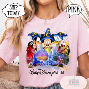May include: Pink t-shirt featuring Mickey Mouse, Donald Duck, Goofy, and Pluto in wizard hats, with a purple sphere, a castle, and the words "Walt Disney World". The shirt has the text "SHIP TODAY" and "PINK".
