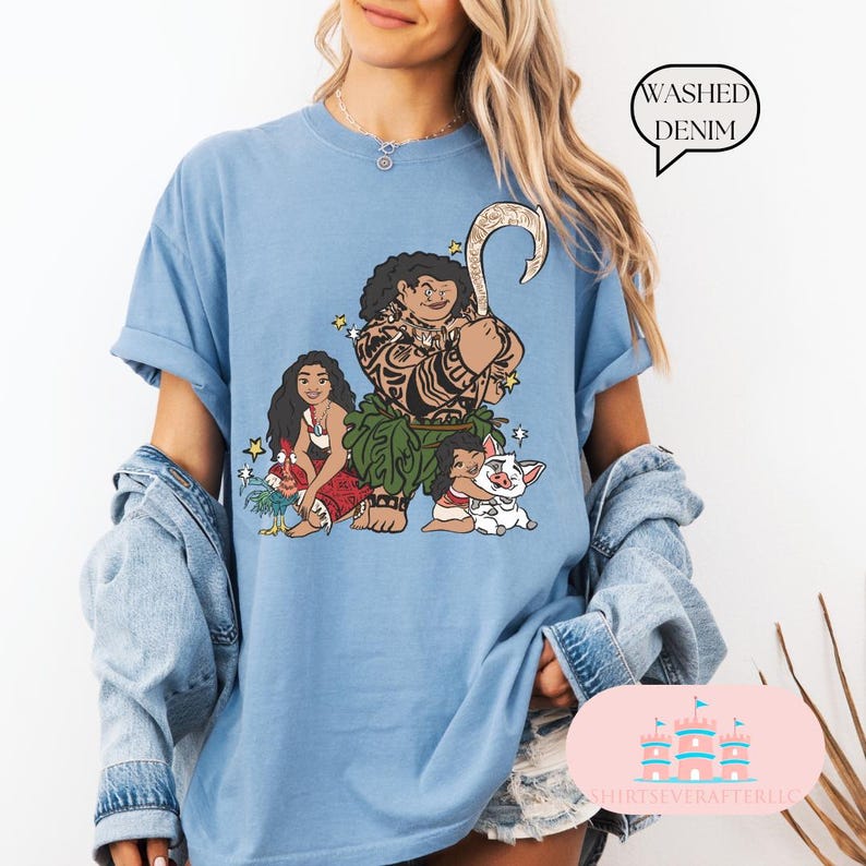 May include: A blue t-shirt with a graphic of Maui, Moana, and Pua from the Disney movie Moana. The shirt is made of washed denim.