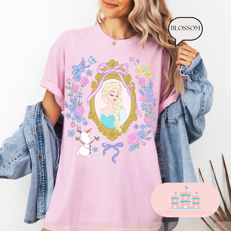 K&ouml;nnte beinhalten: Pinkes T-Shirt mit einem floralen Design, das eine Prinzessin in einem goldenen Rahmen, einen Schneemann und das Wort "Blossom" zeigt.